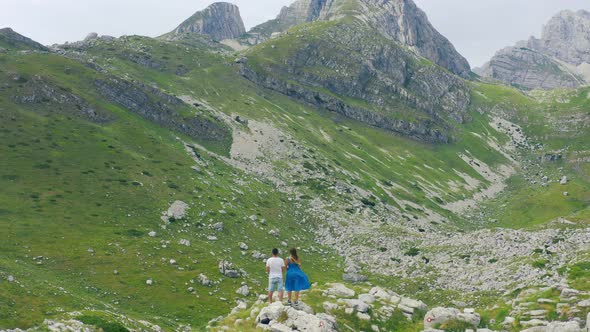 Back View of Young Tourist Couple Holding Hands on Rocky Mountain Top Enjoying Fantastic Panorama alt