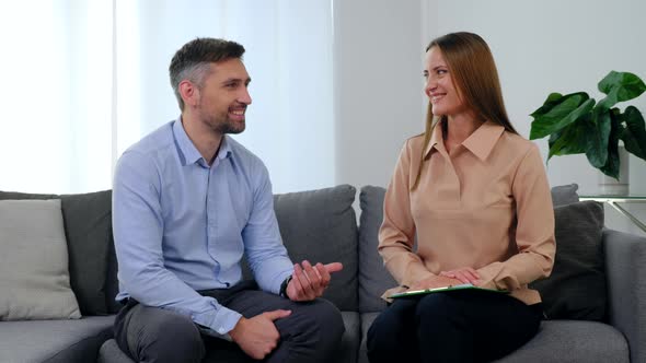 Man Patient and Woman Psychologist Talking and Turn to Camera with Smile alt
