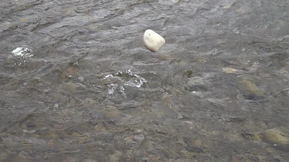 White stone slowly falls into the water of the mountain river, slow motion