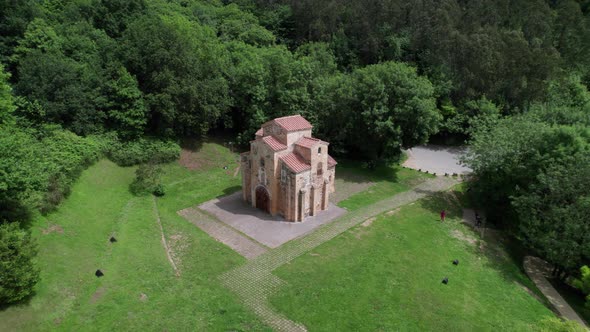 Drone zoomed out revealing a large ancient pre-Romanesque church in the middle of a green forest. Da alt