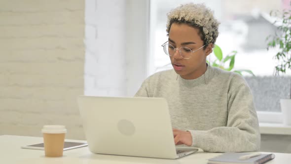 African Woman Looking at Camera While Using Laptop in Office alt