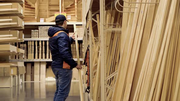 Young Guy Chooses Wooden Beams in Building Materials Store. alt