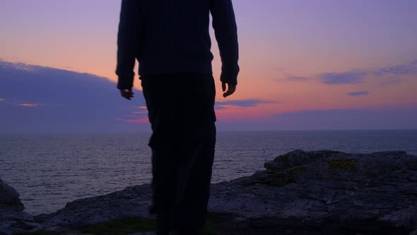 Young Man Walks to a Rocky Sea Shore to Wait for the Sunrise. Stands Upright. Silhouette alt