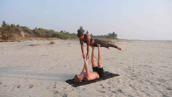Fit Sporty Couple Practicing Acro Yoga with Partner Together on the Sandy Beach alt