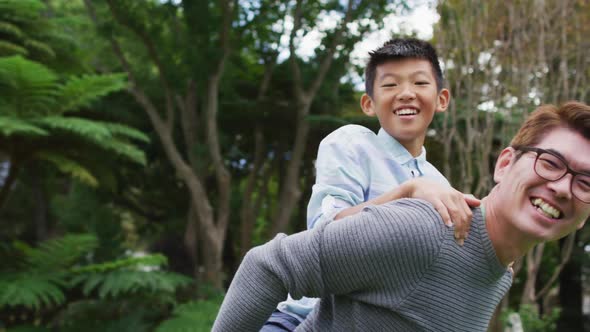 Smiling asian father piggy backing happy son having fun in garden together alt