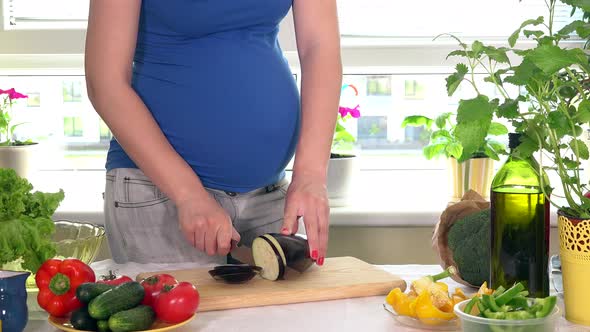 Pregnant Woman Belly and Hands Slicing Eggplant Vegetable with Knife for Salad