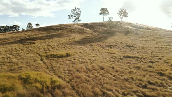 Dramatic forward tracking aerial shot at pace that glides over a hill to reveal a beautiful, lush la alt