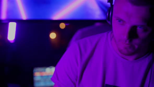 Man DJ working in club in neon lights indoors. Caucasian male person using headphones to mix music alt