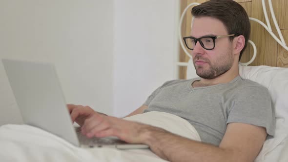 Beard Young Man Get Surprise on Laptop in Bed alt