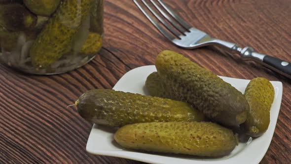 Pickled cucumbers in bowl on wooden rustic table and jar of pickles.