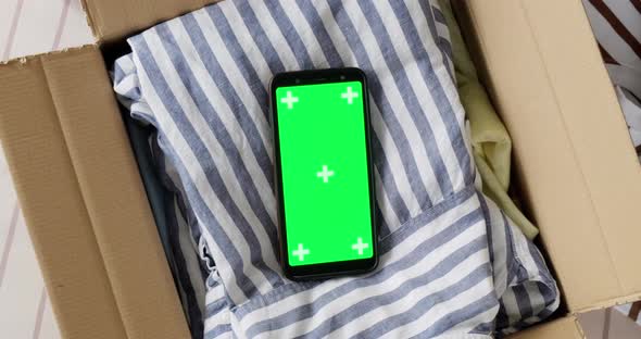 Top view of phone green screen mockup in box with used clothes. alt