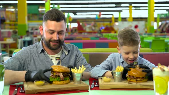 Young Father and His Little Son Eating Burgers at Restaurant alt