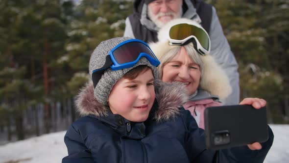 Pensioners with Grandson in Forest Smiling Male Child Filming Video on Smartphone Camera Together