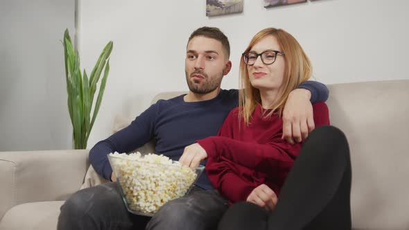Couple watching TV while eating popcorn alt