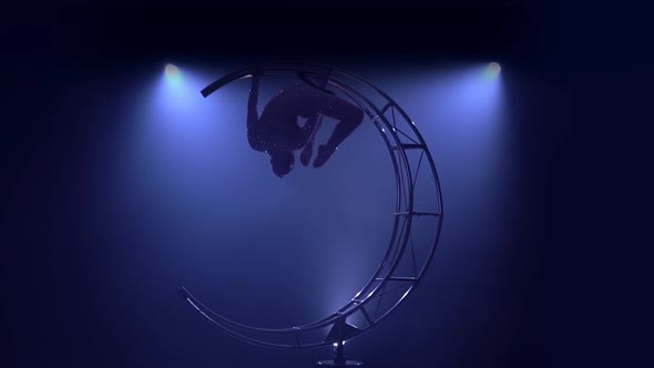 Graceful in a Brilliant Costume Performs Tricks on a Special Design in a Dark Room alt