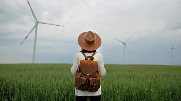 Young woman in a hat and with a backpack in a field with windmills alt