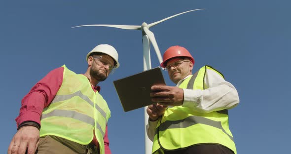 Two Engineers Watch Information About a Windmill in the Background Turning Their Heads Back alt