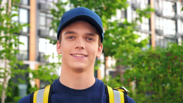 Close Up Smiling Young Man Courier Delivery with Thermal Backpack Looking Camera alt