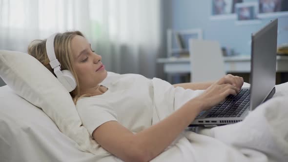 Smiling Girl Lying in Bed, Communicating With Friends in Social Media on Laptop alt