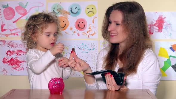 Happy Mother and Daughter Putting Coins Into Piggy Bank