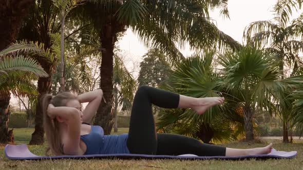 Beginning Fitness Woman is Pumping ABS Exercise on Yoga Mat in Public Park alt