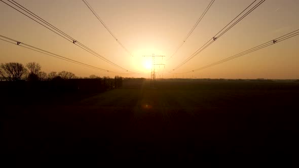 Aerial pullback along Powerlines, silhouette of Electric tower during sunset alt