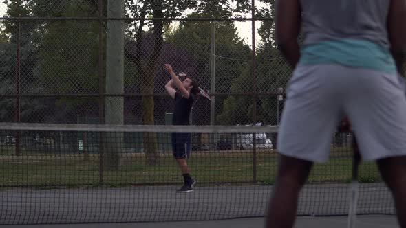 Caucasian Male Unsuccessfully serves his black Male opponent at a local community tennis match, Ball alt