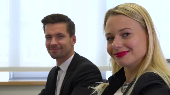 Two office workers, man and woman, work on computers and smile at the camera - closeup alt