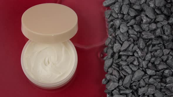 Mineral Water Breaks Through Rocks Surrounding Jar of Moisturizing Beauty Cream