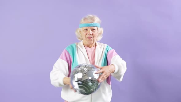 Happy Senior Woman in White Sportswear Holding Discoball in Hands on Purple alt