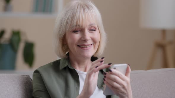 Mature Elderly Mature 60s Caucasian Woman with Phone Female Smiling Uses Mobile App at Home Buys alt