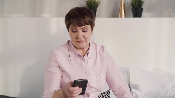 Senior Attractive Grandmother Is Sitting on Sofa and Texting Online on Slow Motion.
