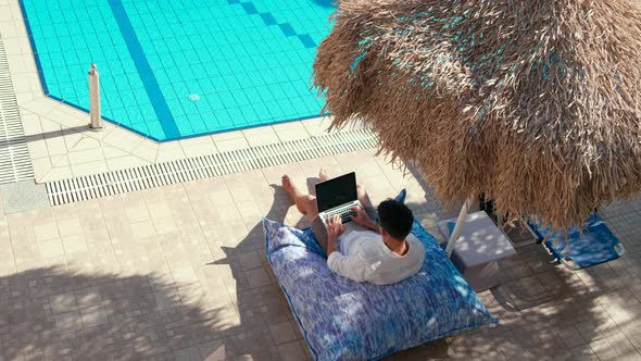 Man Works on Vacation Using Laptop By Swimming Pool in Hotel Resort in Summer