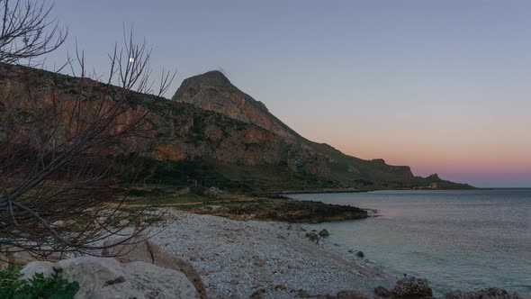 Timelapse of twilight to golden sunrise with moon setting behind mountain of Monte Cofano at mediter alt