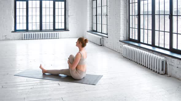 Pretty slim woman in stylish light grey tracksuit does half lord of fishes pose alt