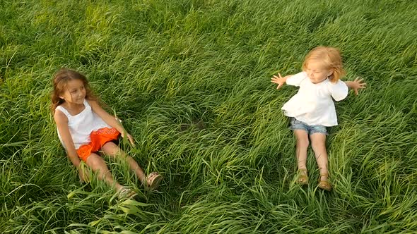Children Falling on Green Grass and Lying. Cute Children Walking on Green Grass