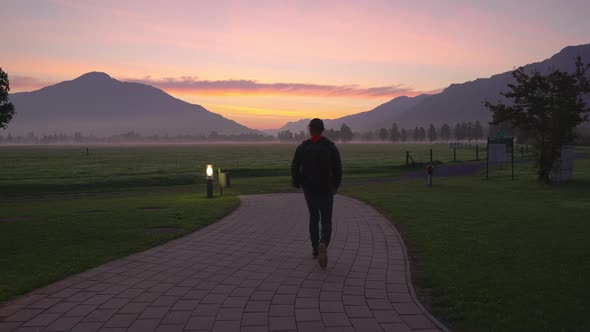 Man Walking Along Footpath Towards Misty Landscape At Dawn alt