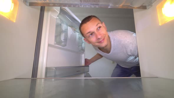 the man opens the refrigerator, sniffing and plugging his nose alt
