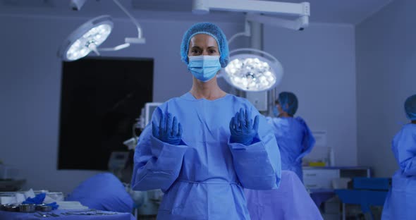 Portrait of caucasian female surgeon wearing face mask and protective clothing in operating theatre alt