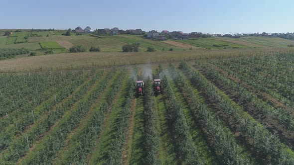Aerial view of tractors irrigating an apple plantation alt