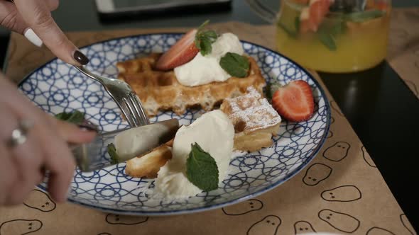 Women's Hands Appetizing Cut Waffles with Fruit and Dip in Cream