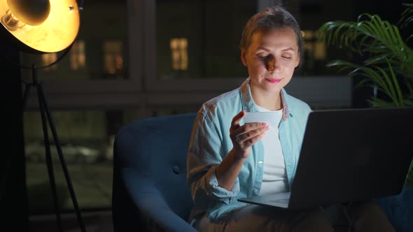 Woman is Sitting in the Armchair and Makes an Online Purchase Using a Credit Card and Laptop at alt