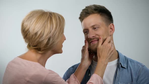 Mother Pinching Cheeks to Infantile Adult Son Under Mom Overprotection, Care alt