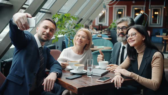 Group of Colleagues Male and Female Taking Selfie in Restaurant Using Smartphone Camera alt