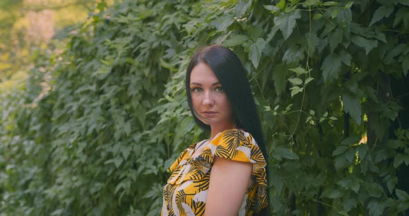 Young and beautiful woman in the park on the background of green leaves alt