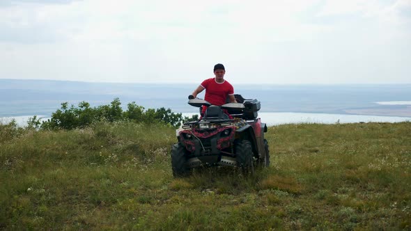 Man in a Black Cap and Red T-shirt on a Colored ATV Rides alt