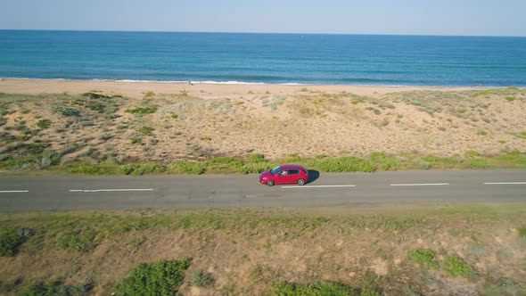 Red Car Driving Slowly on Coastal Asphalt Road Along the Black Sea Shore alt