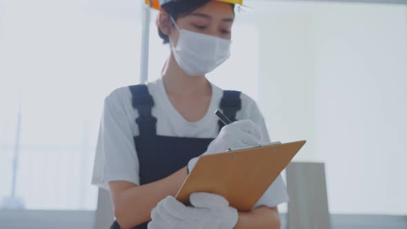 Asian construction worker girl wear face mask due to Covid 19 and yellow hard hat, examine and check alt