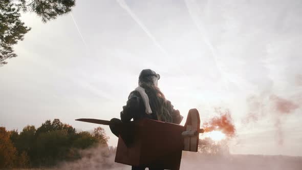 Low Angle Camera Follows Little Girl Running in Fun Cardboard Plane Pilot Costume with Color Smoke alt