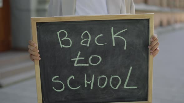 Woman Arms Holding and Raising Schoolboard with Text Message Back to School on Street Close Up alt